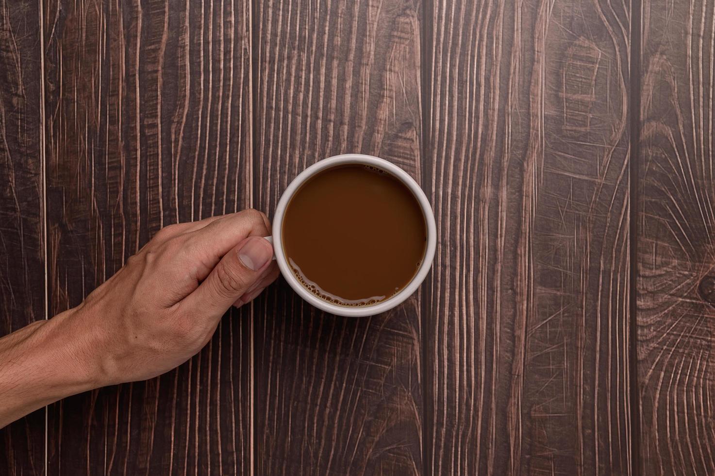 Hand, die eine Kaffeetasse auf einem hölzernen Hintergrund hält foto