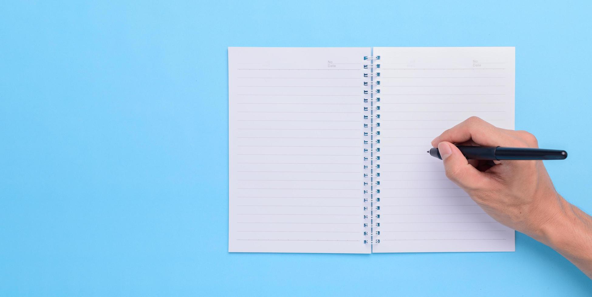 Hand, die einen Stift hält, um auf einem Notizbuch auf blauem Hintergrund zu schreiben foto