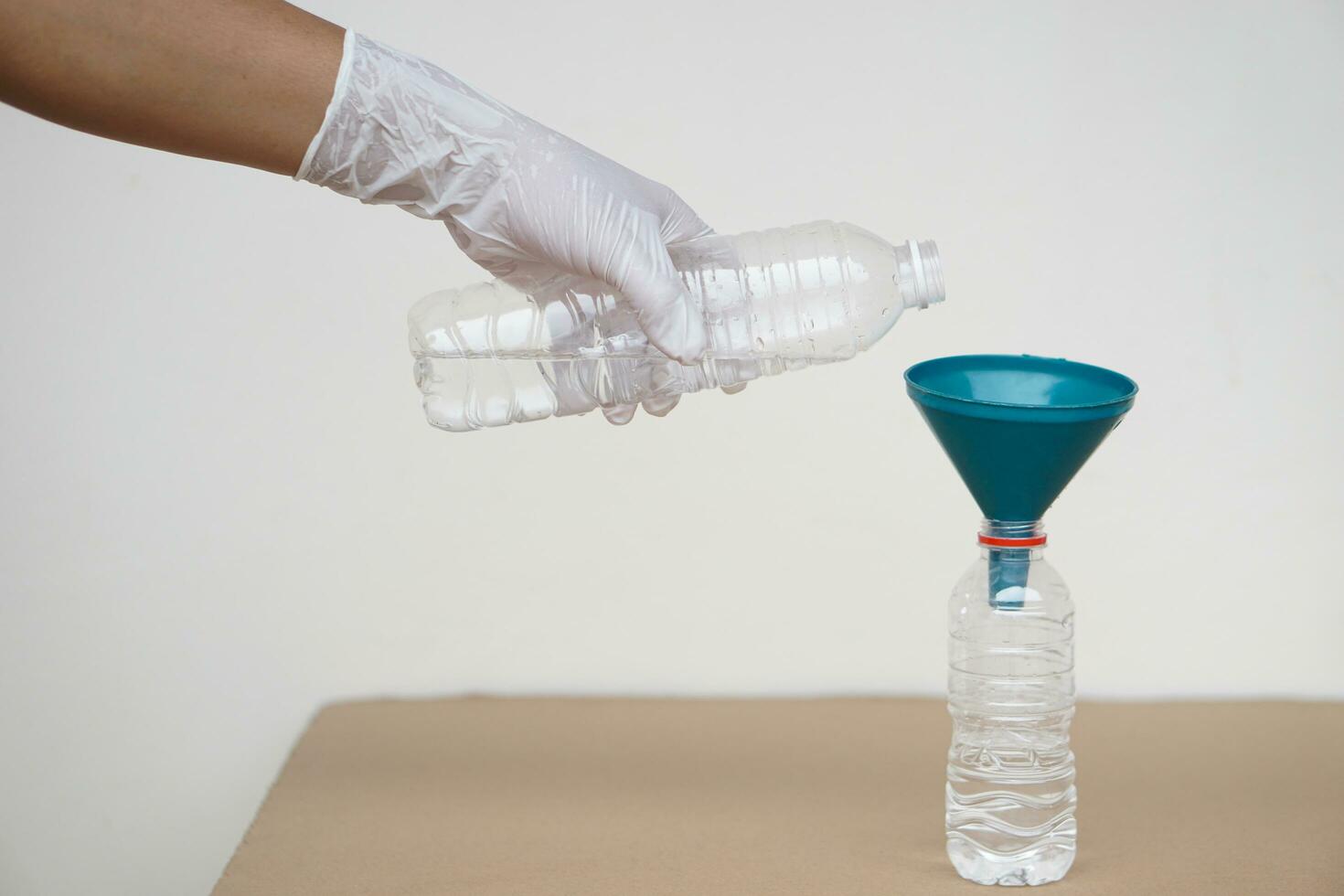 Nahansicht Hand tragen Handschuh hält Flasche von Wasser zu gießen Wasser in Flasche zu tun Wissenschaft Experiment. Konzept, Wasser Menge Messung zum Mischen chemisch Substanzen. foto