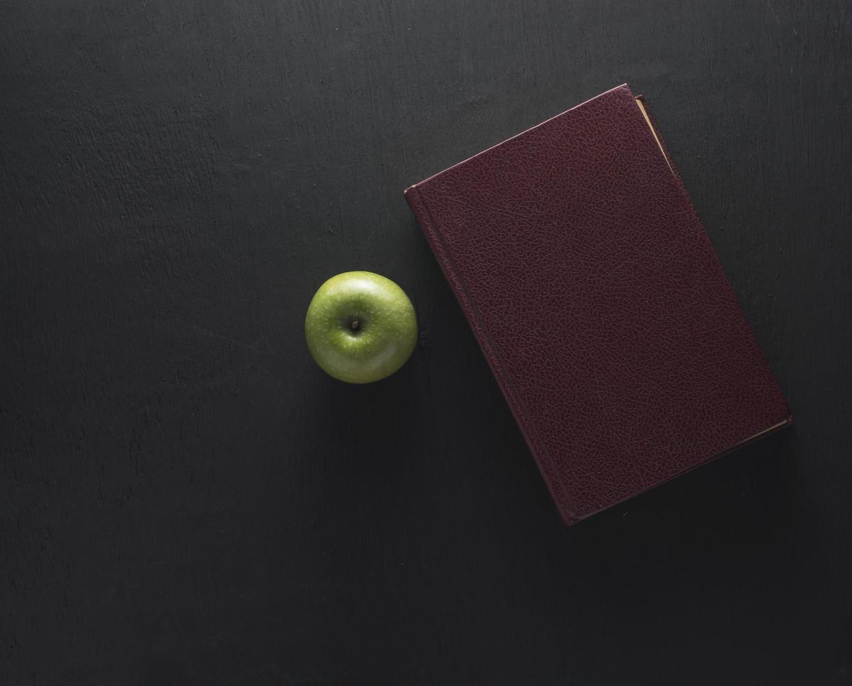 Draufsicht des grünen Apfels mit altem Buch auf schwarzem Holzhintergrund foto