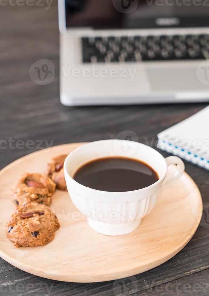 schwarzer Kaffee und Kekse mit Laptop und Notebook auf dem Tisch foto