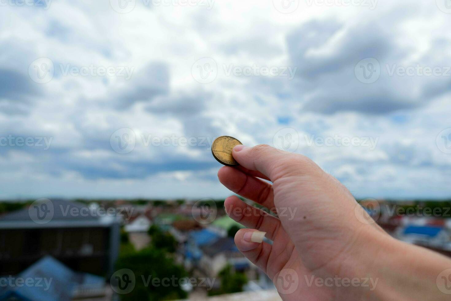 einer Hand hält ein Münze. zu Show seine verwenden von Geld das Hintergrund ist das Stadt. und das Blau Himmel Abdeckungen foto