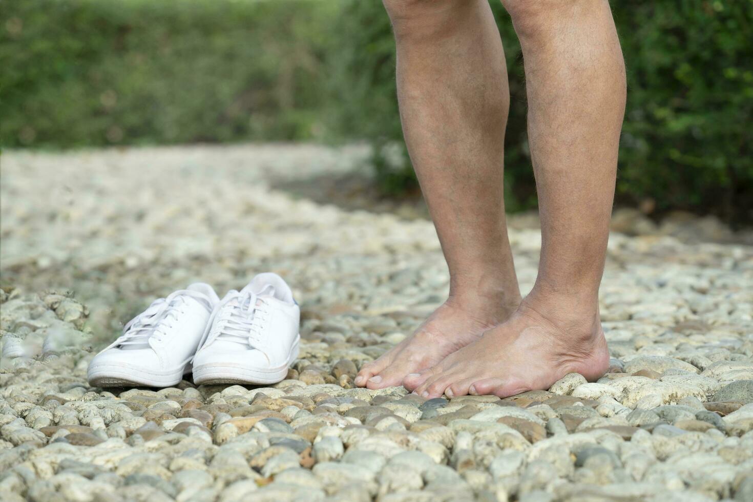 das alt Mann dauerte aus seine Schuhe zu gehen barfuß auf Fuß Reflexzonenmassage Weg beim das Öffentlichkeit Park, Konzept zum Risiko oder Vorteil von Gehen barfuß foto