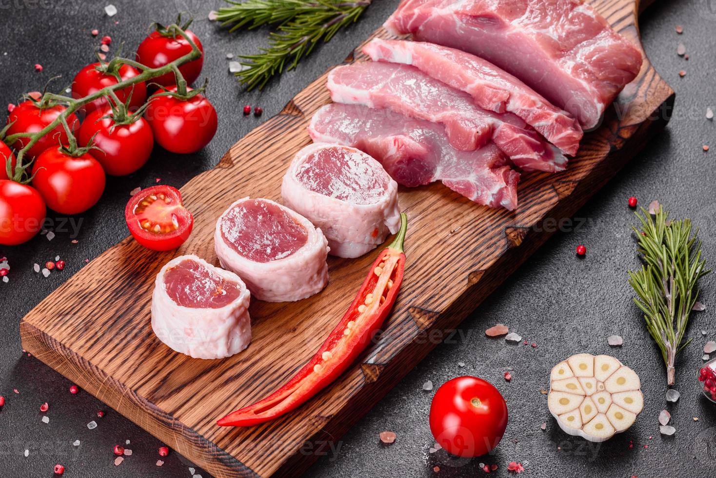 frische Stücke Schweinefleisch kochfertig auf dunklem Hintergrund in der Küche foto