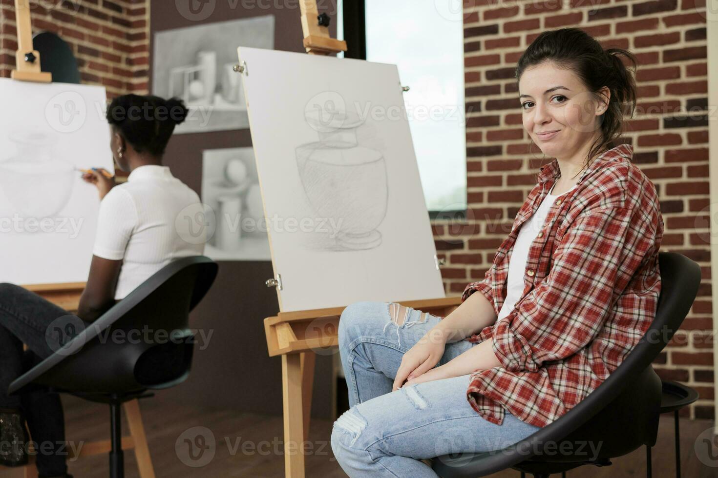 glücklich jung Frau Sitzung beim Staffelei im Klassenzimmer und lächelnd beim Kamera, genießen Spaß Zeichnung Klasse mit Freunde, Lernen Skizzierung Techniken beim Gruppe Kunst Klasse. angenehm kreativ Hobby foto