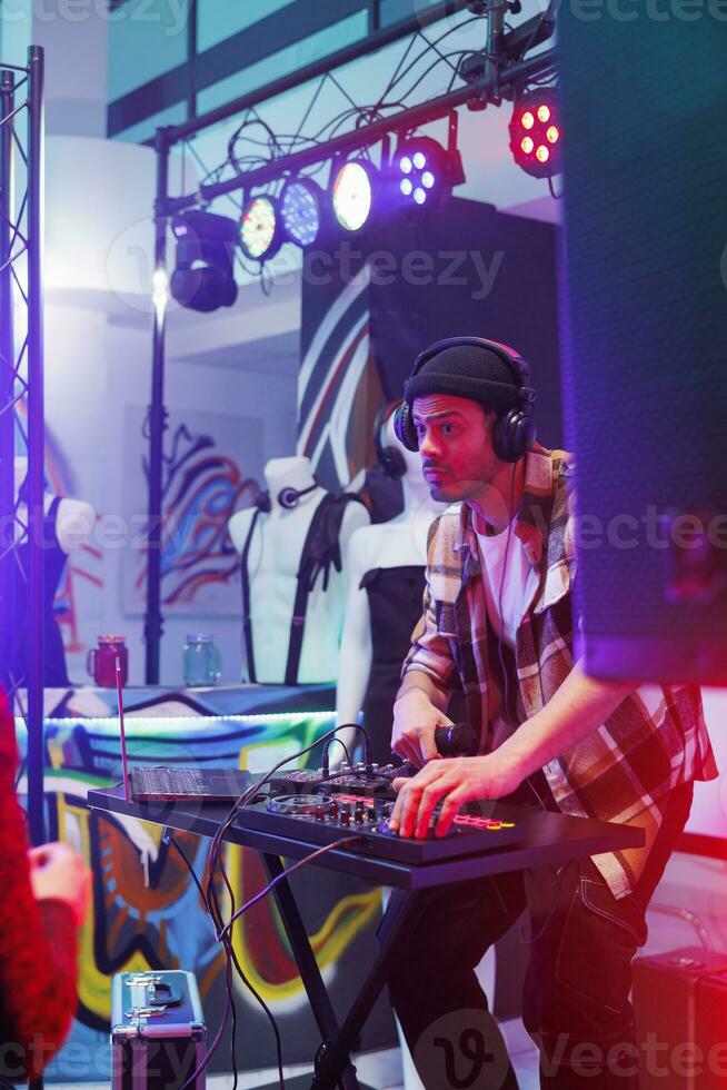 dj Mischen elektronisch Musik- auf Digital Regler beim Party im Nachtleben. jung Mann Musiker im Kopfhörer durchführen mit Rührgerät Konsole Panel auf Bühne mit Scheinwerfer beim Konzert im Verein foto