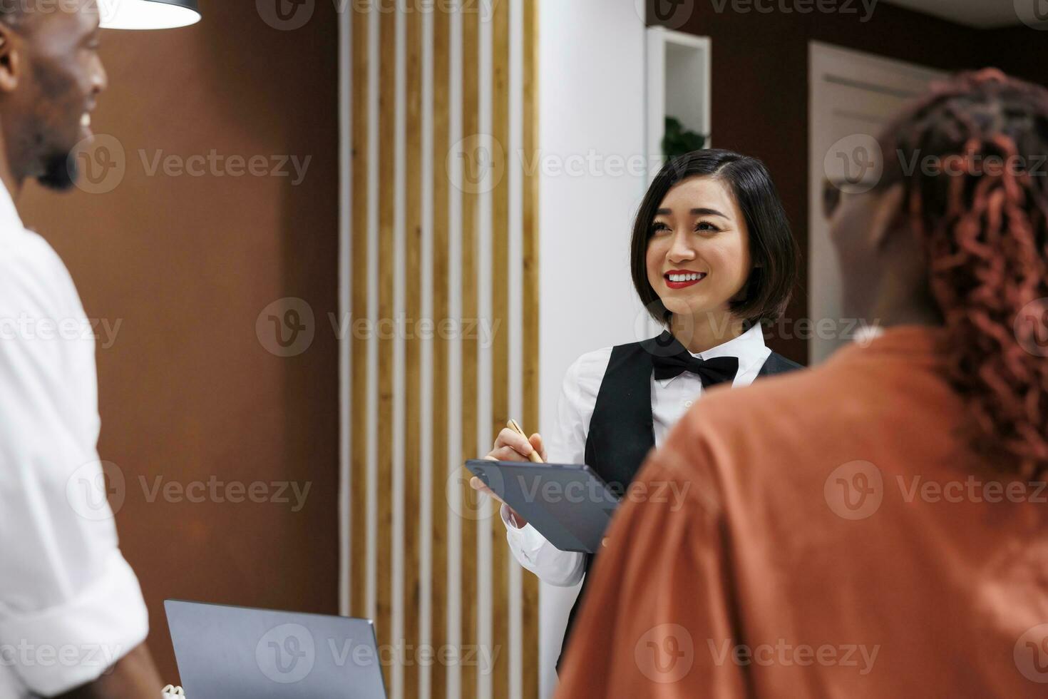 asiatisch Frau Schreiben prüfen im bilden auf Tablette, Portion Gäste mit Anmeldung Prozess beim Hotel Rezeption. weiblich Mitarbeiter Arbeiten mit Computer zu zur Verfügung stellen Luxus Unterkunft. foto