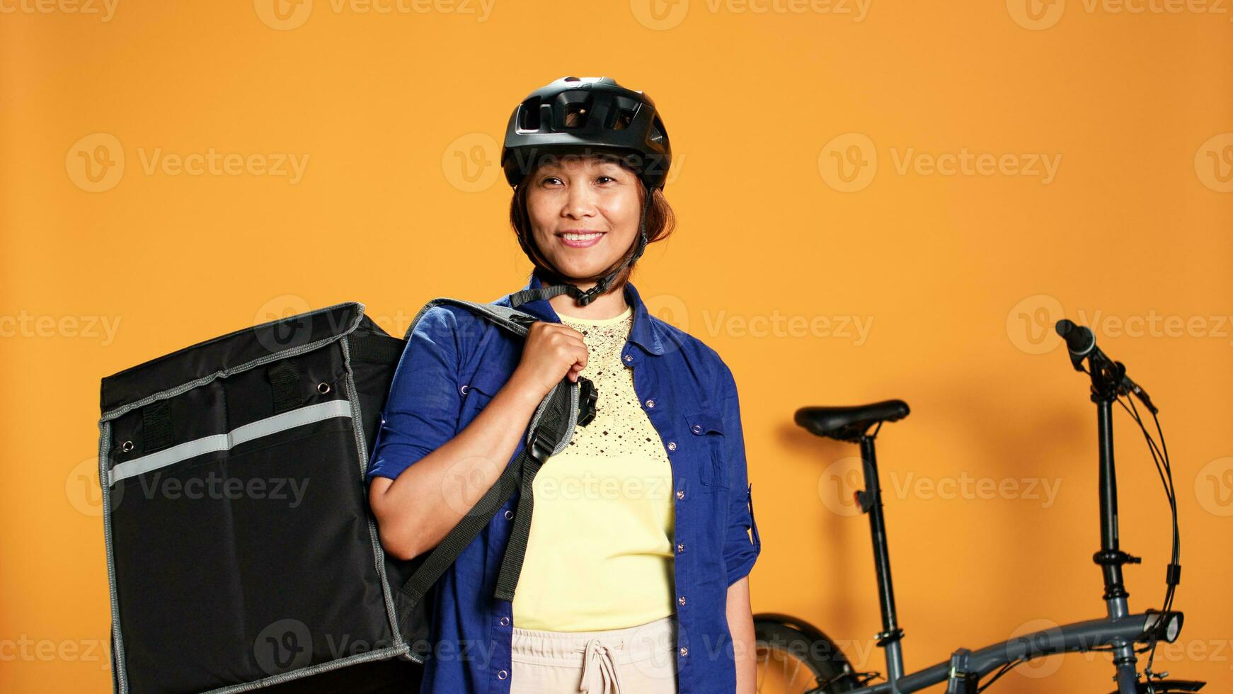 Porträt von heiter optimistisch bipoc Kurier mit Fahrrad zu Transport Lebensmittel bestellen zu Klient. Lieferung Teil Zeit Arbeiter tragen schützend Helm und Thermal- Rucksack zum Essen foto