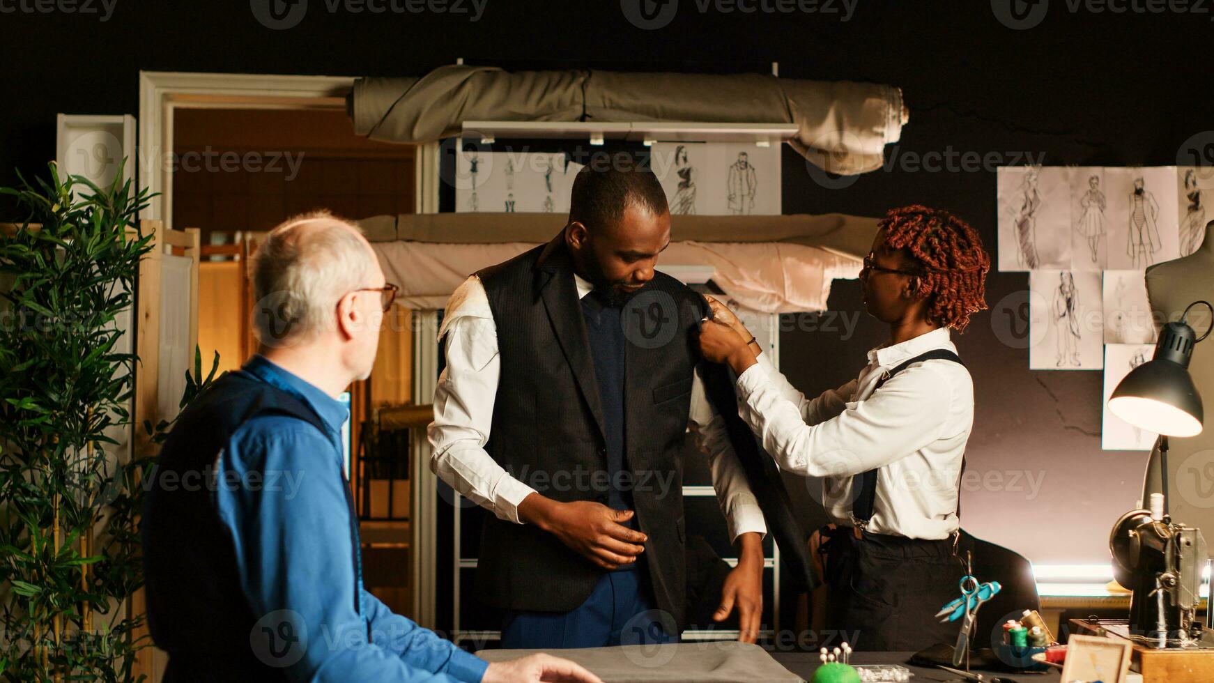 jung Kunde versuchen auf passen Jacke im Atelier, Herstellung sicher es passt mit das richtig Messungen. erfahren Schneider und Assistent Entwerfen Benutzerdefiniert gemacht Blazer, passend zu im Werkstatt. foto