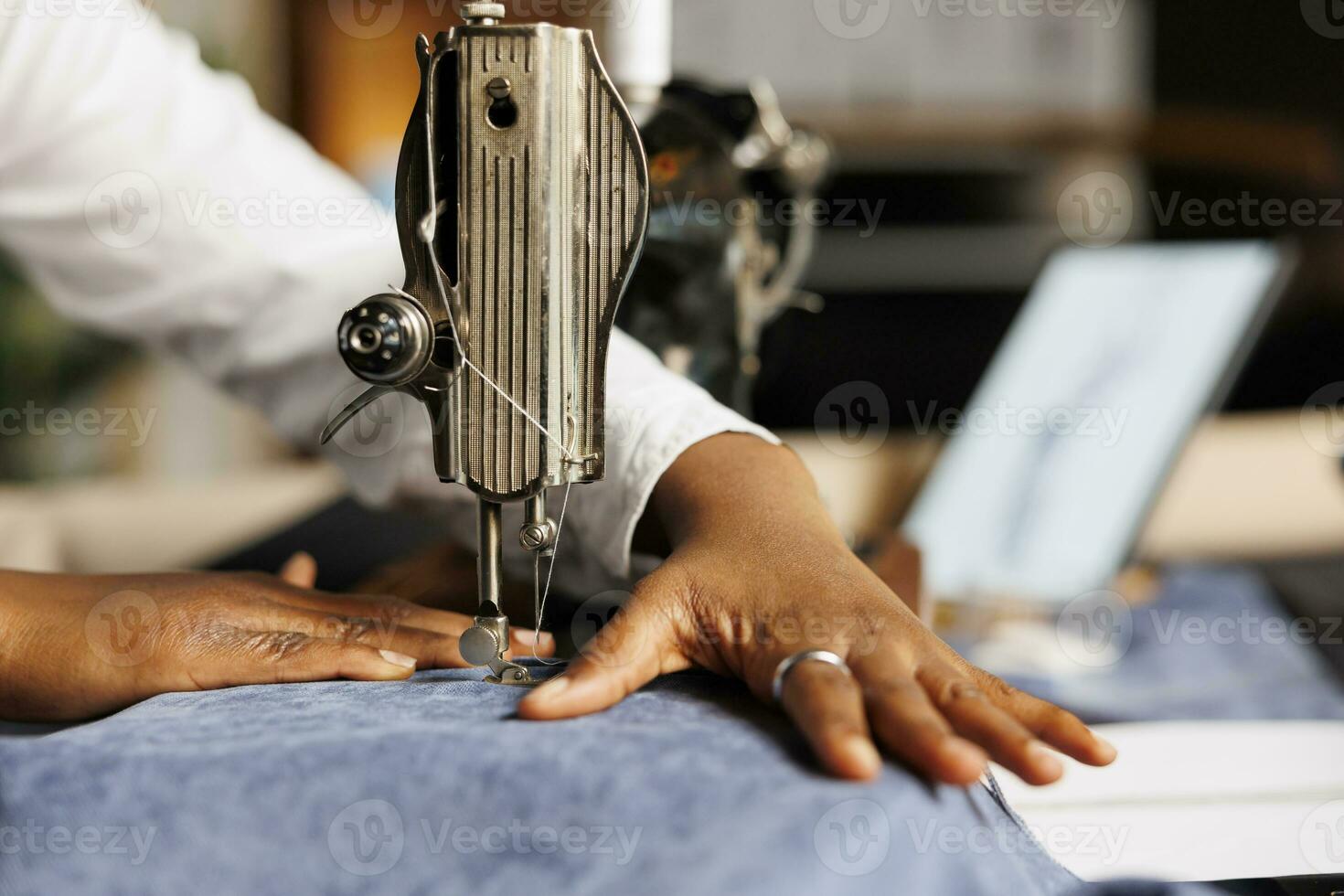 extrem schließen oben von afrikanisch amerikanisch Näherin mit industriell Nähen Maschine auf Stoff Material im Atelier Geschäft Arbeitsstudio. Schneider Schneiden Kleidung Kleidungsstück Stück, Herstellung maßgeschneidert Outfits foto