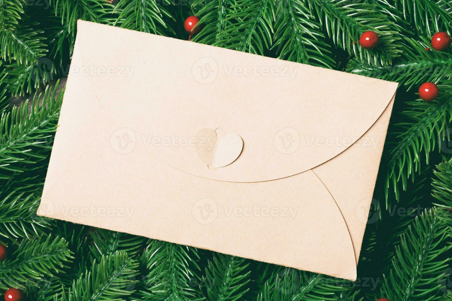Blick von oben auf den Umschlag, der mit einem Rahmen aus Tannenbaum auf Holzhintergrund dekoriert ist. neujahrszeitkonzept foto