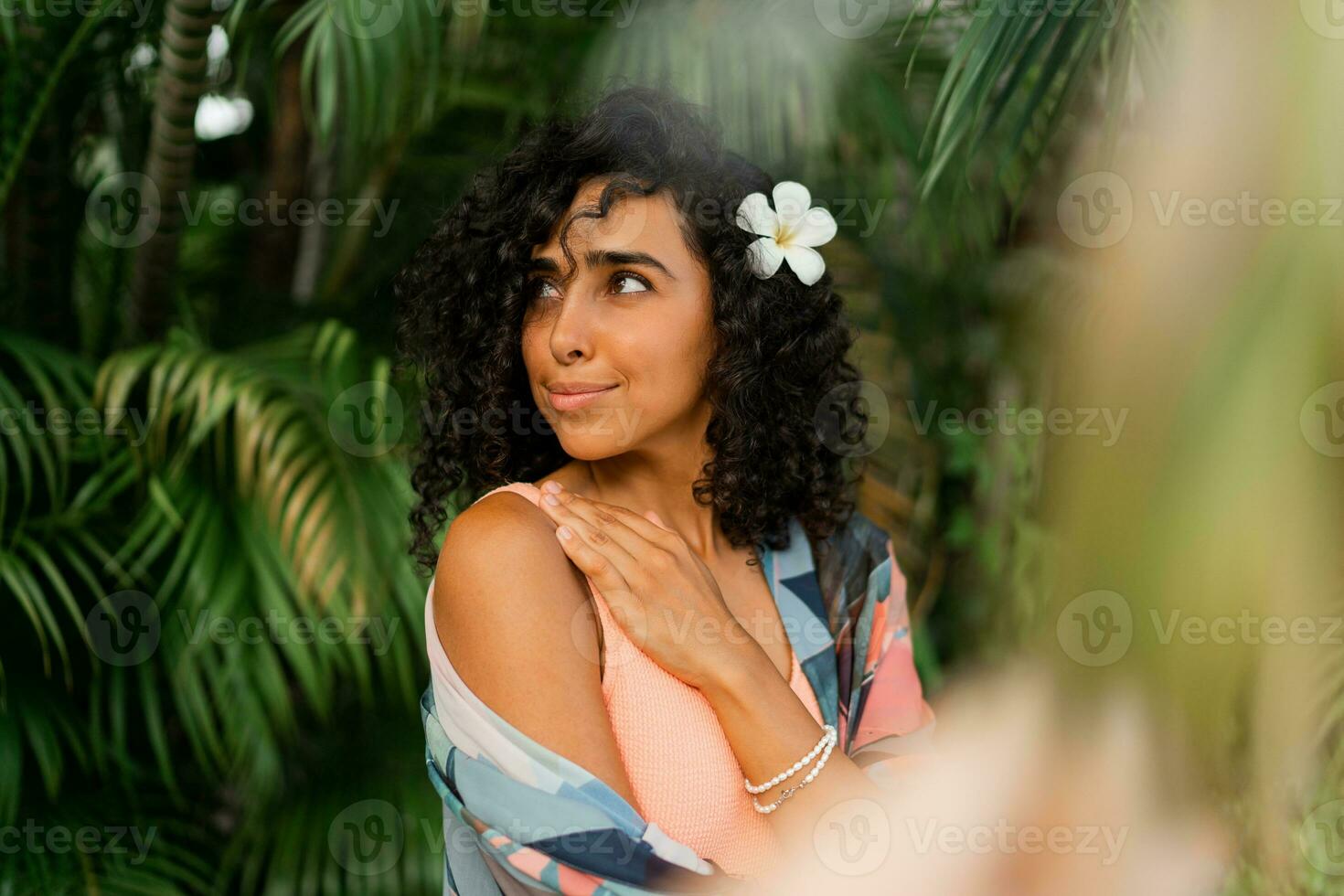 schließen oben Porträt von glückselig Frau mit Plumeria Blume im Haare nach Spa im Luxus Erholungsort. tragen Boho tropisch Outfit. foto