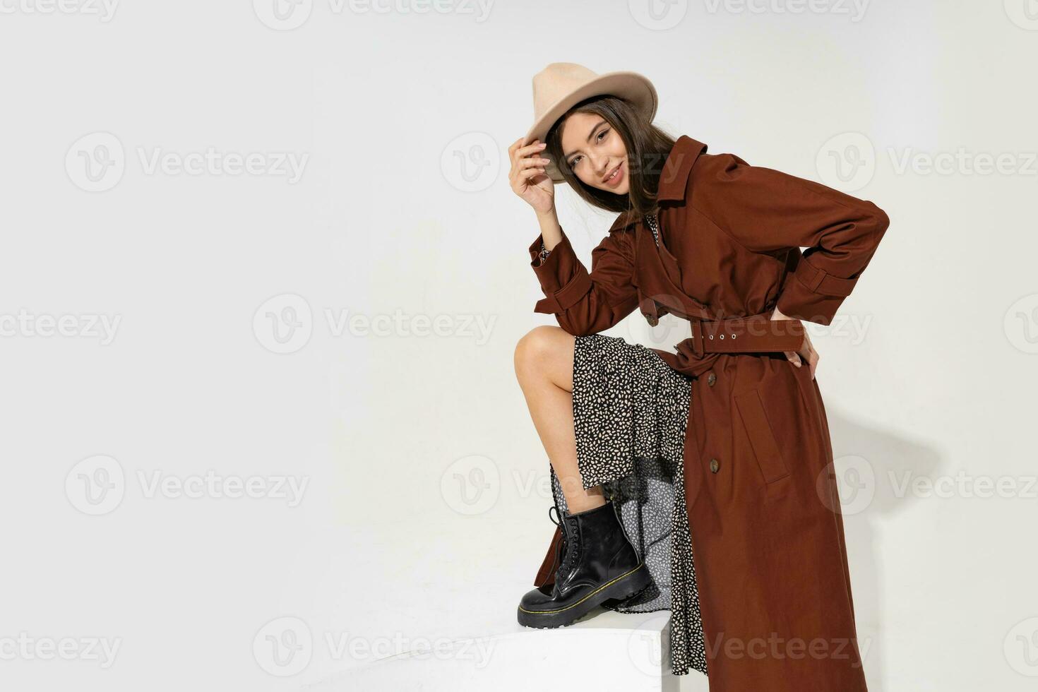 modisch jung Frau im Hut und modisch Winter Mantel posieren im Studio auf Weiß Hintergrund. zeigen Knöchel Stiefel im schwarz Leder. foto