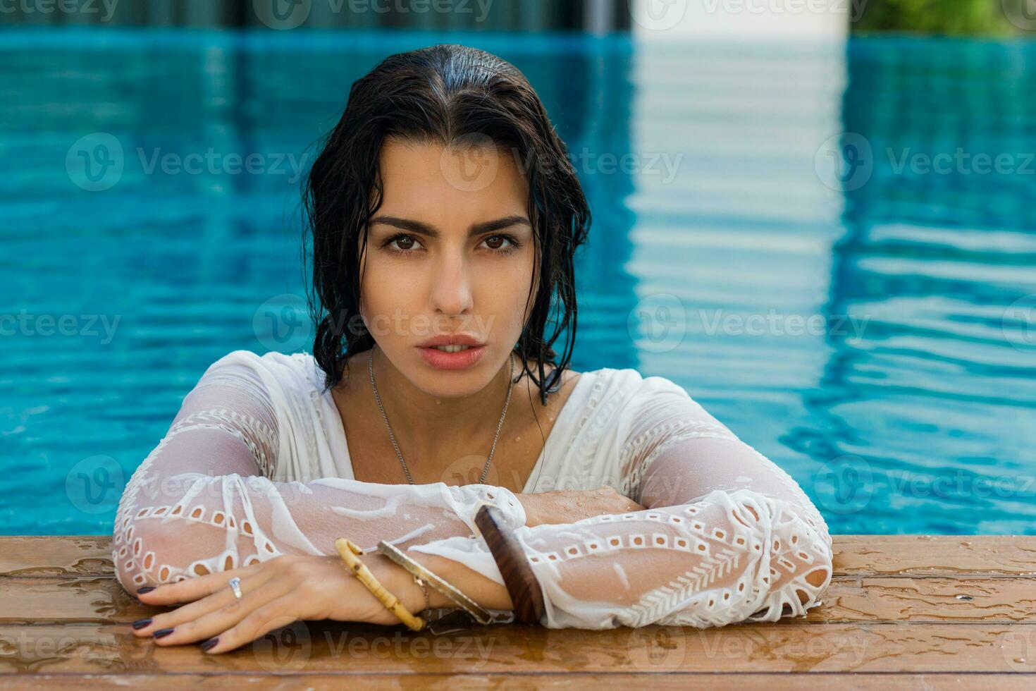 schön sinnlich Frau mit perfekt bräunen Haut, im nass Boho Outfit posieren im Schwimmen Schwimmbad foto