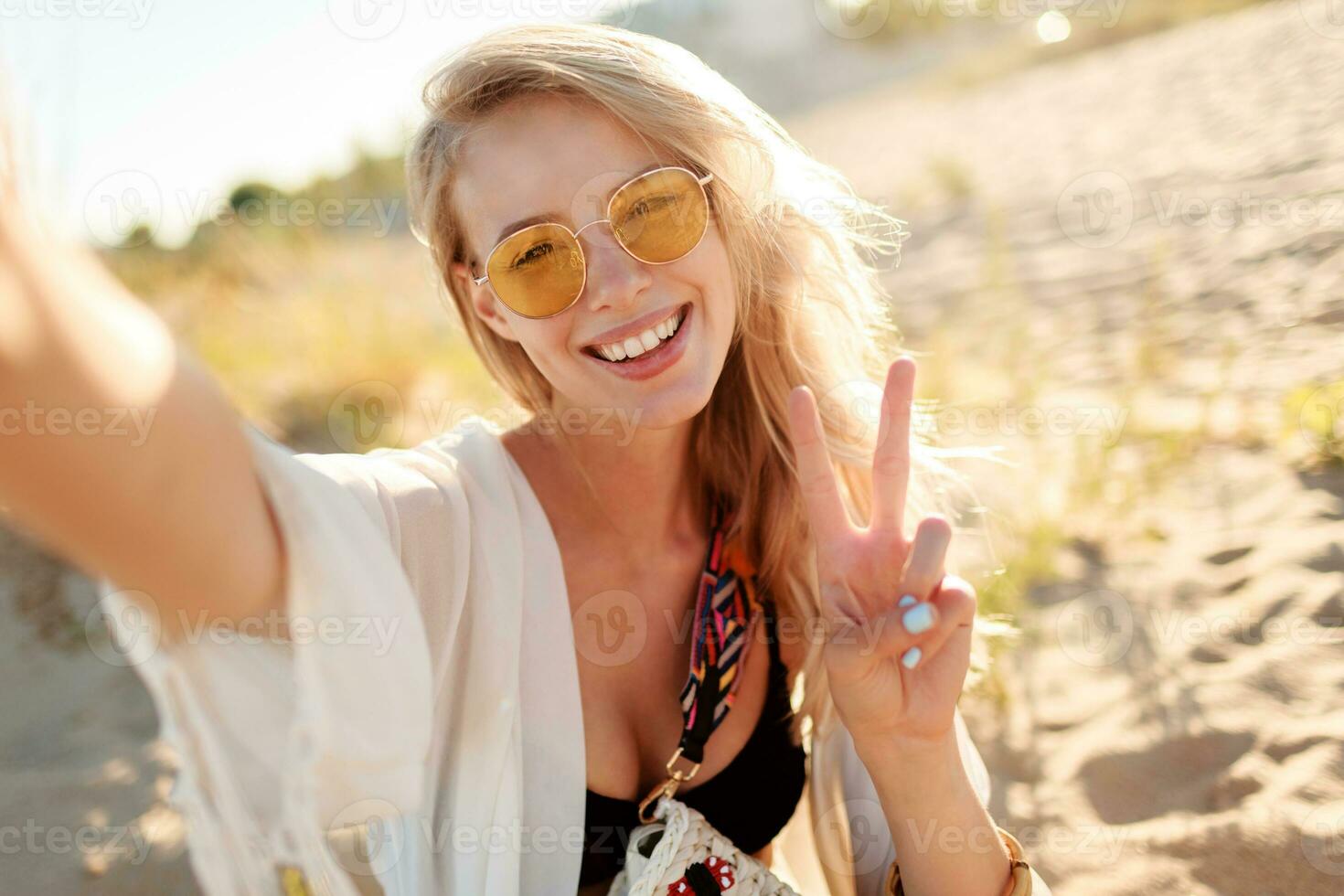 schließen oben Porträt von lächelnd Frau mit blond Haare Herstellung selbst Porträt auf sonnig Abend Strand. foto