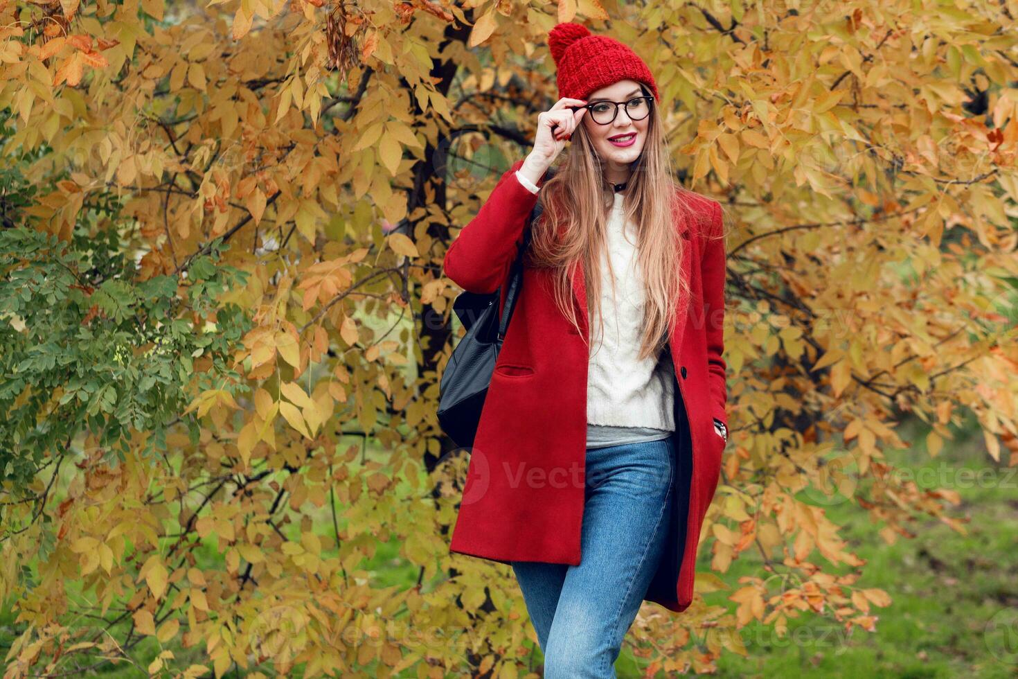 lächelnd blond Frau mit lange Haare Gehen im sonnig Herbst Park im modisch beiläufig Outfit. foto