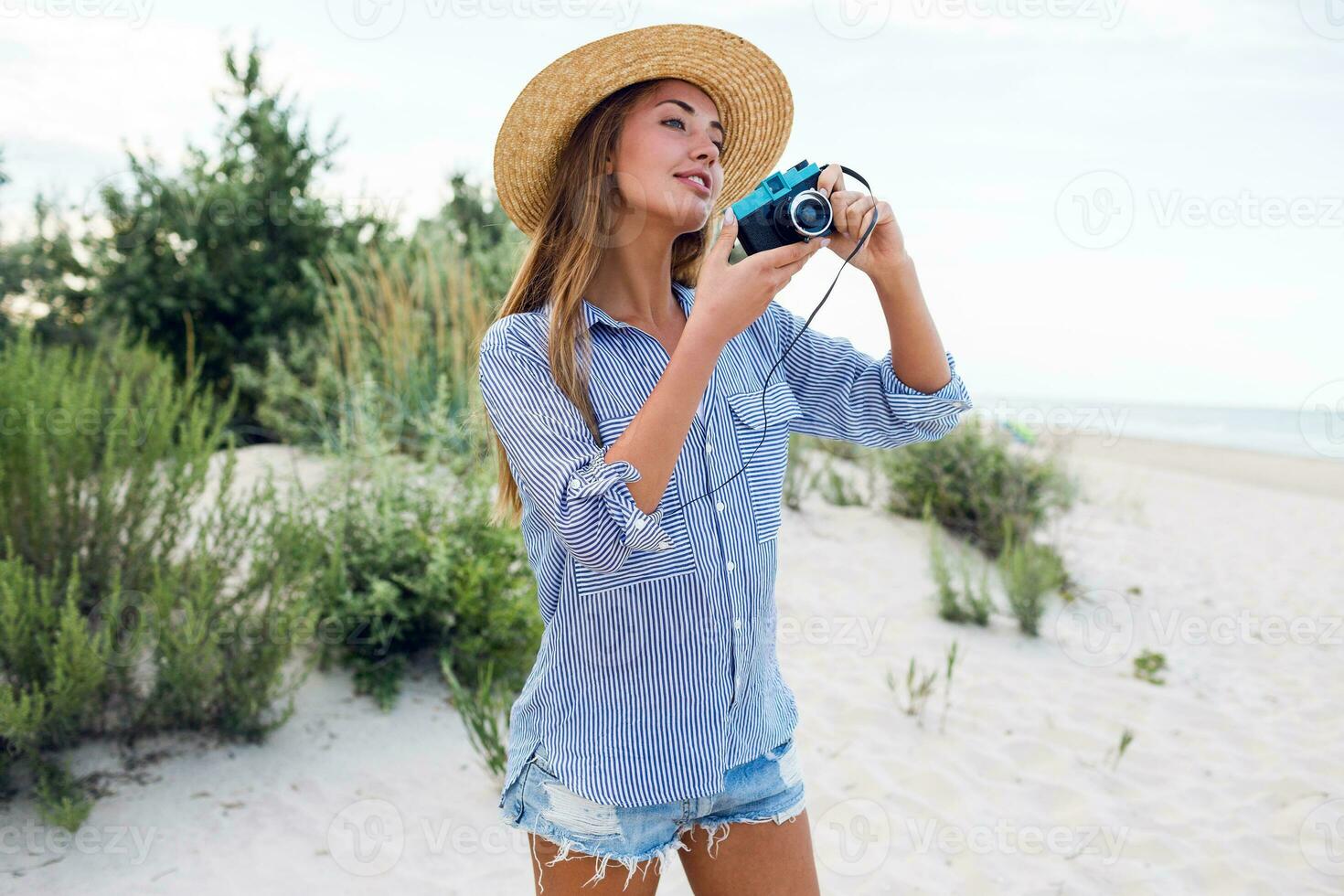 schön jung Mädchen im Stroh Hut auf Kopf Herstellung Bild durch Kamera auf Ferien Zeit in der Nähe von Abend Strand. foto
