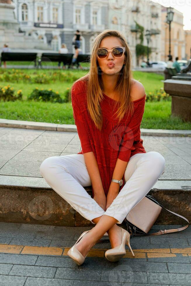 modisch Weiß Frau im Sweatshirt Sitzung auf das Straße im Stadt Center. stilvoll Sonnenbrille. Herbst Stimmung. foto