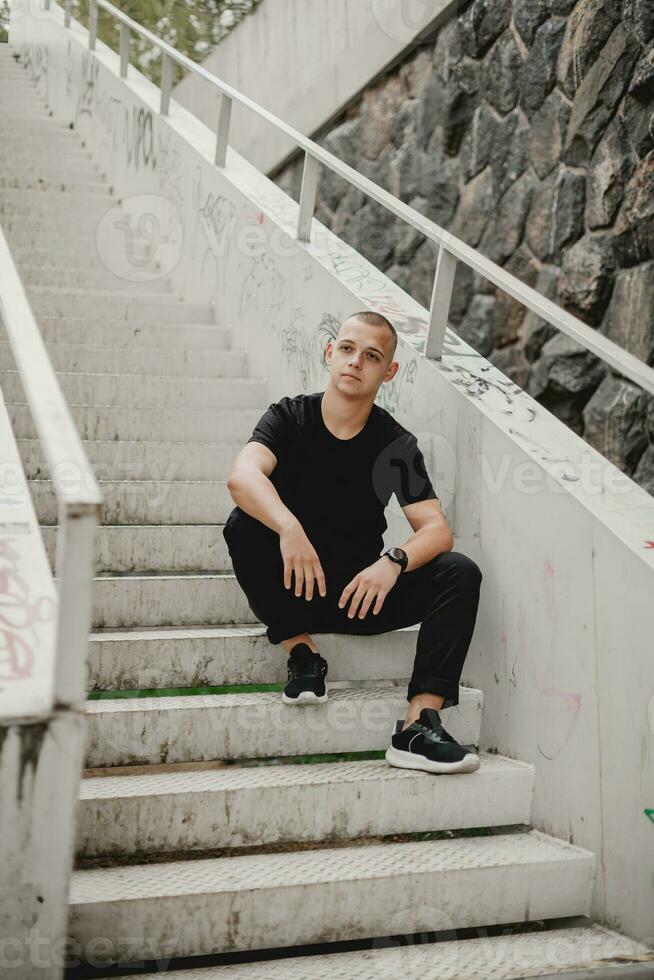 Stadt Einsamkeit. nachdenklich jung Mann ruht auf städtisch Treppe. städtisch Grübler. stilvoll jung Kerl sitzt und spiegelt auf Treppe. Grübeln Kerl ruht auf städtisch Treppe foto