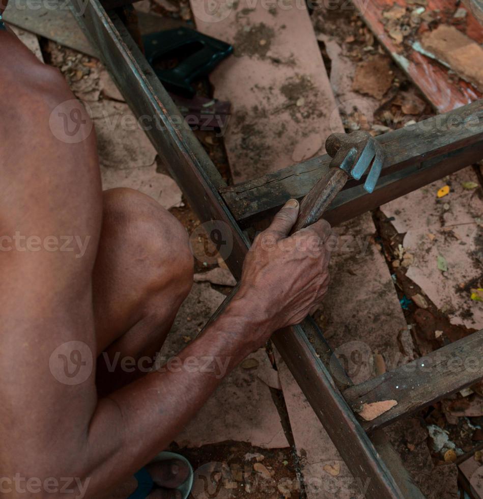 alter älterer Mann, der ein handgefertigtes Holzprodukt mit einem Hammer repariert. foto