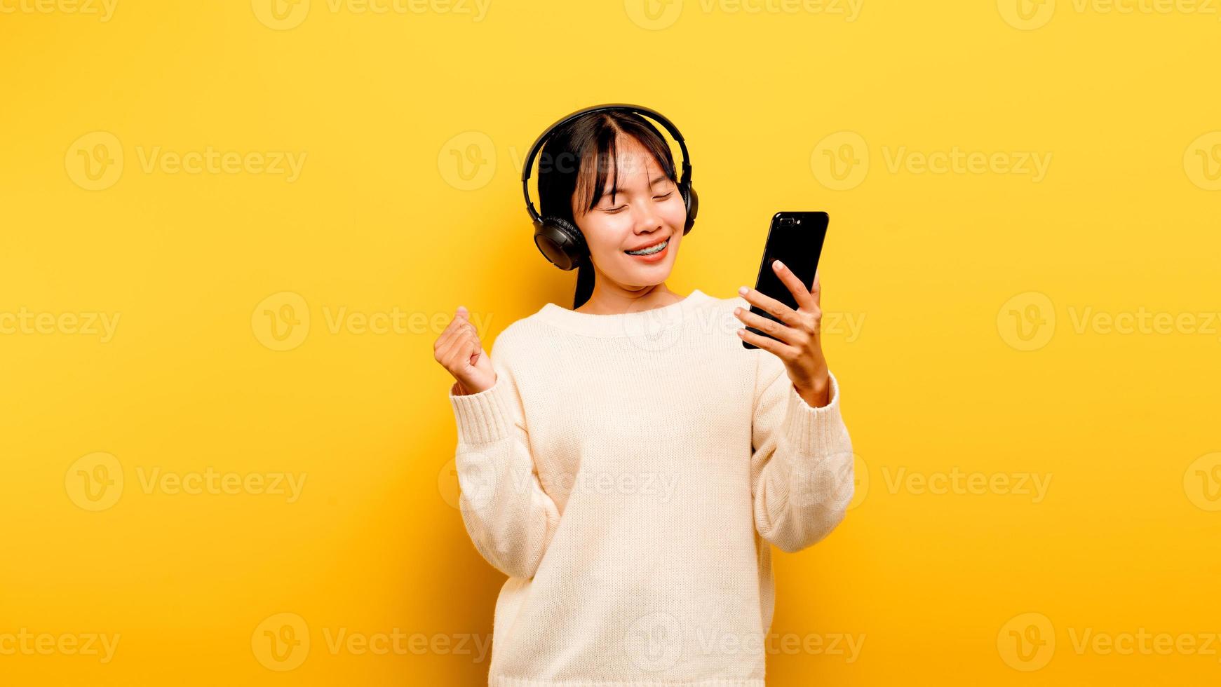 asiatische Frau, die glücklich das Telefon benutzt und Musik hört foto