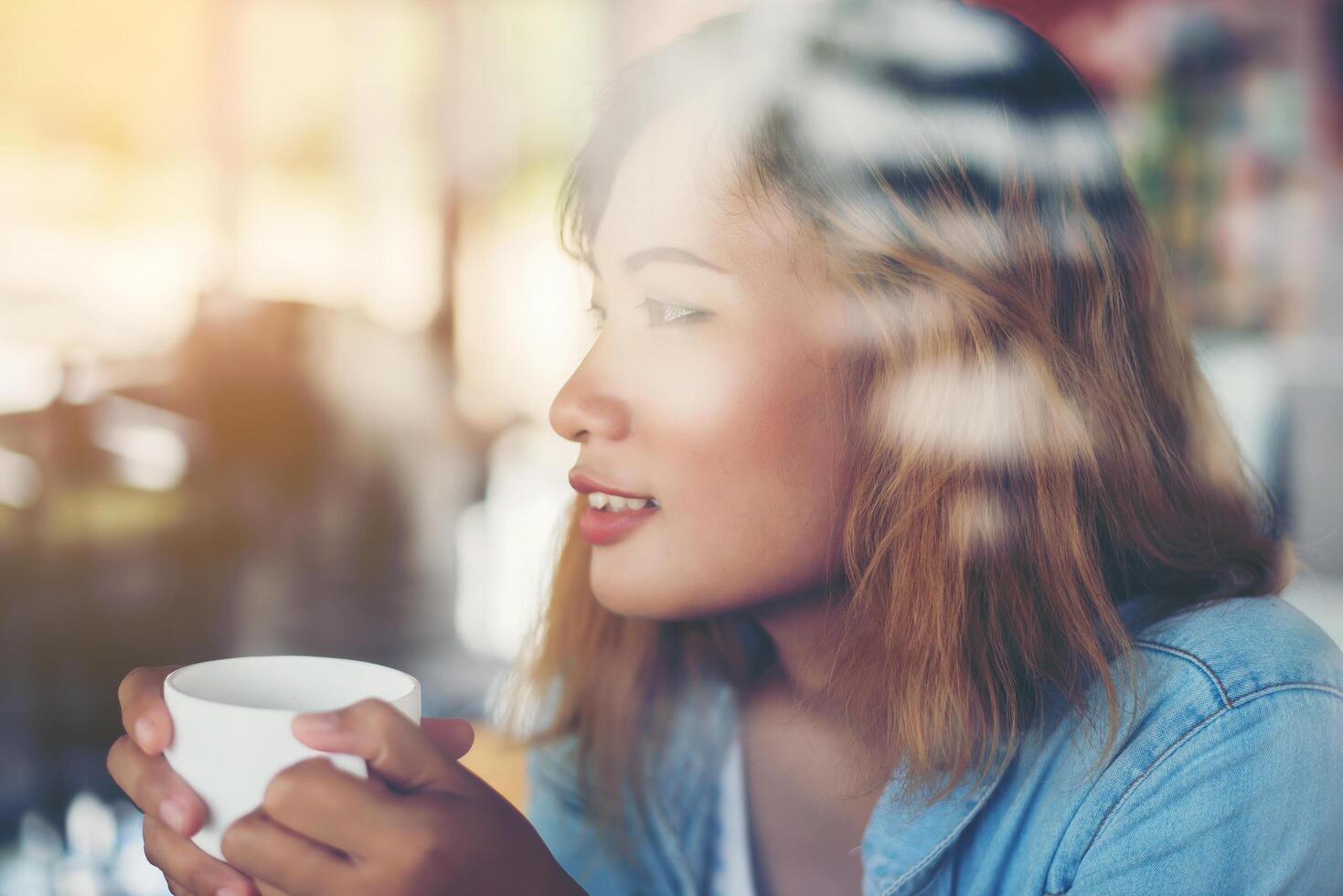 Hipster-Frau, die eine Tasse Kaffee hält und im Café arbeitet foto