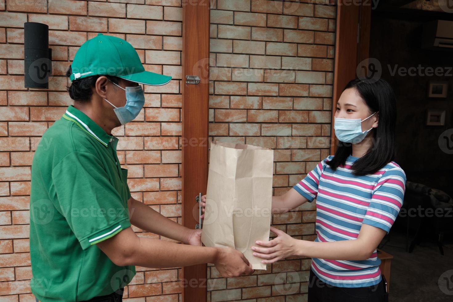 Liefermann mit Gesichtsmaske gibt einer asiatischen Frau ein Paket. foto