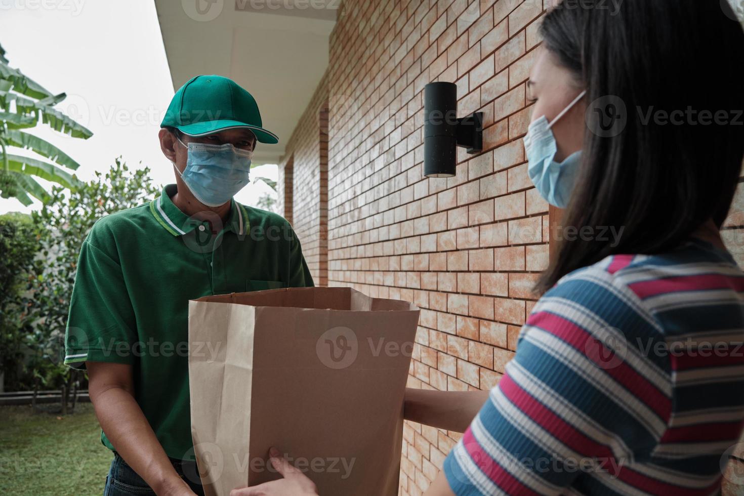 Liefermann mit Gesichtsmaske gibt einer asiatischen Frau ein Paket. foto