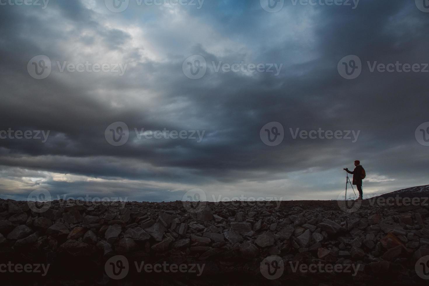 Silhouette eines Fotografen oder Reisenden mit Stativ auf Stein stehend foto