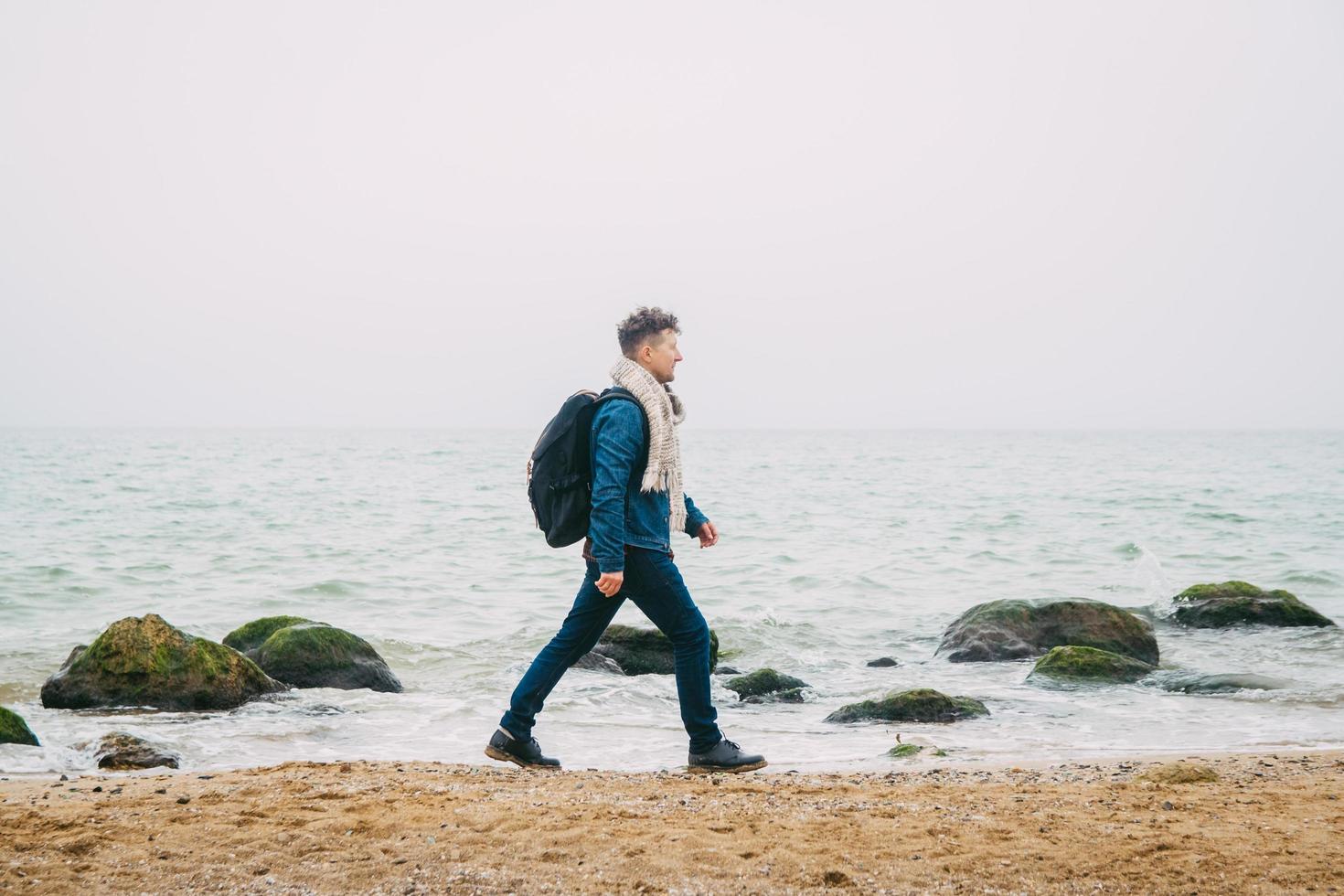 Mann mit Rucksack, der in der Nähe eines Felsens gegen ein schönes Meer steht foto