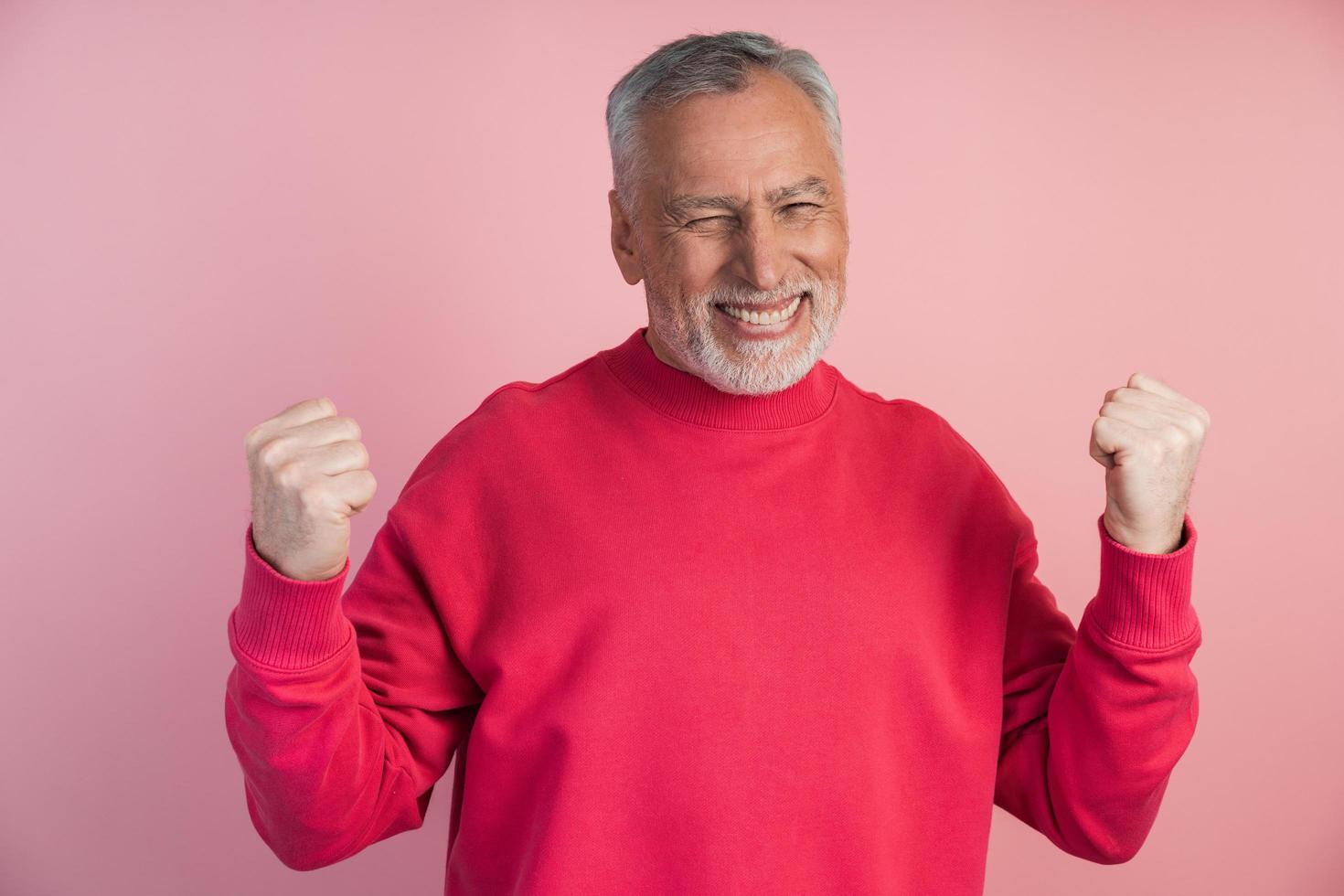 fröhlicher, älterer Mann, der auf einem rosa Hintergrund posiert foto