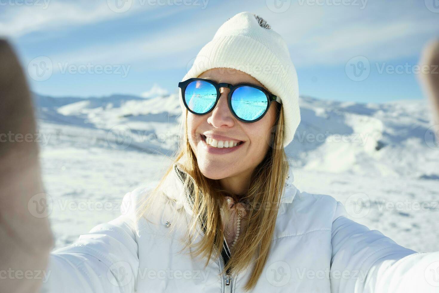 heiter Frau im Sonnenbrille nehmen Selfie im schneebedeckt Platz foto