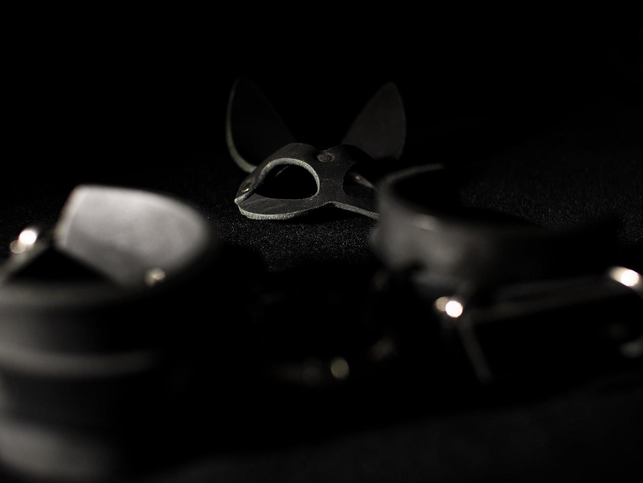Lederhandschellen und eine Hasenmaske auf schwarzem Hintergrund. Fetisch Spielzeug foto