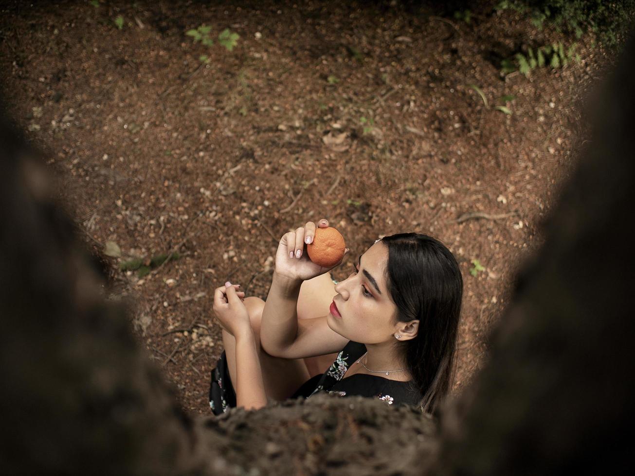 Aussehen eines Mädchens, das in der Nähe eines Baumes sitzt und eine Mandarine in der Hand hält foto