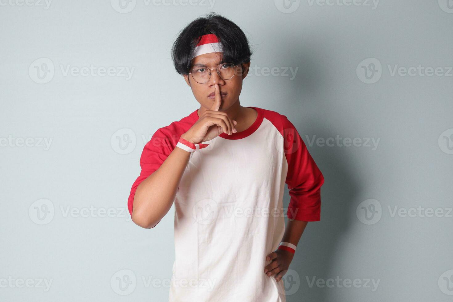 Porträt von attraktiv asiatisch Mann im T-Shirt mit rot und Weiß Band auf Kopf, Flüstern bösartig sich unterhalten Gespräch, Hand auf Mund erzählen Geheimnis Gerücht. isoliert Bild auf grau Hintergrund foto