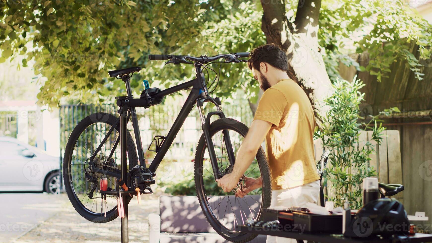 entschlossen männlich Radfahrer vorsichtig entfernen beschädigt Fahrrad Reifen zum ersetzen mit neu. jung kaukasisch Mann Lockerung und Tragen Fahrrad Rad zum des Weiteren Instandhaltung im Zuhause Hof. foto