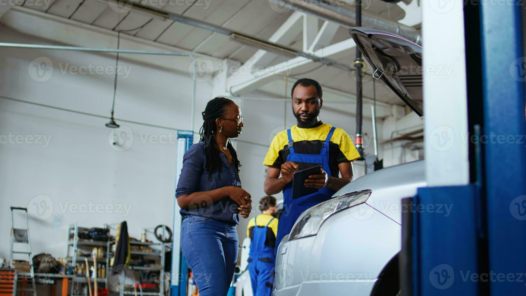 trainiert Handwerker hört zu zu Kunde im Reparatur Geschäft, mit Laptop zu schreiben Nieder Auto Änderungen erforderlich. Experte im Garage mit Klient, Hören zu ihr Anfragen zum Fahrzeug stimmen, Boden Niveau Schuss foto