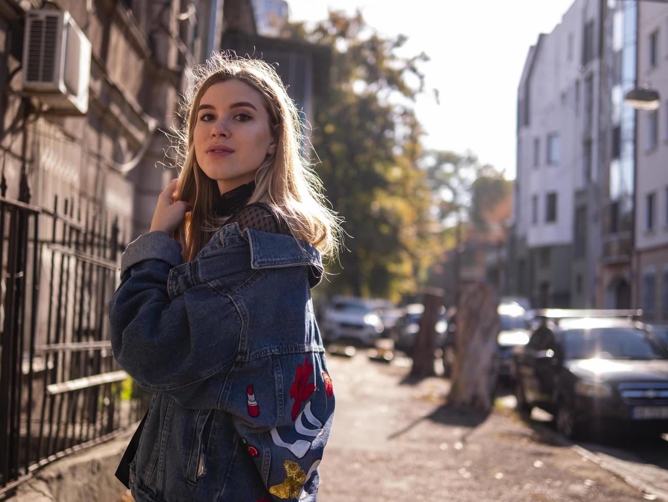 schönes blondes Mädchen steht in einer alten Gasse in einer Jeansjacke foto