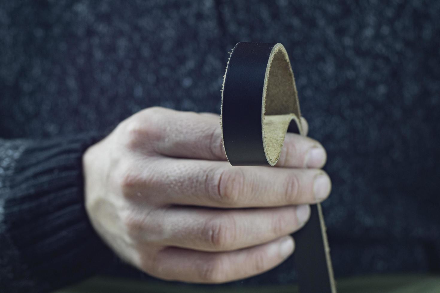 Handwerker hält ein echtes schwarzes Lederarmband in der Hand foto