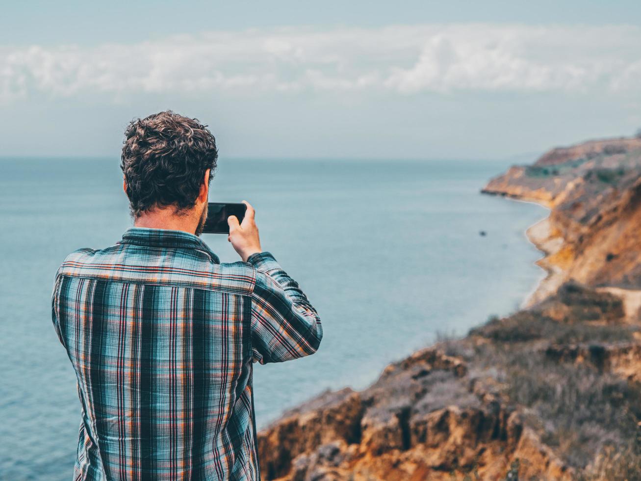 ein Mann macht ein Foto am Telefon und steht auf einem Felsen