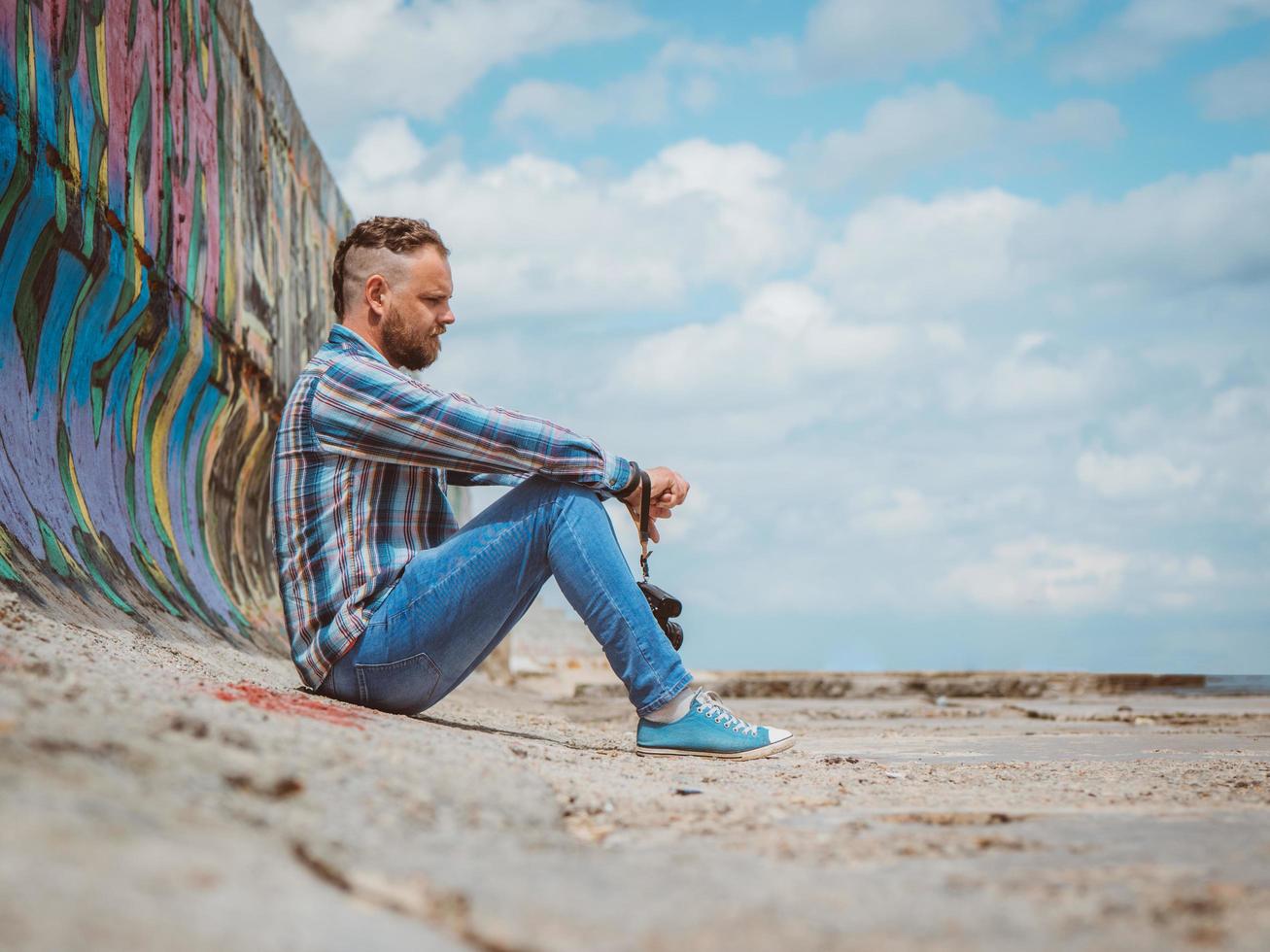 bärtiger Hipster-Mann mit Mohawk sitzt auf einem Betonpier foto