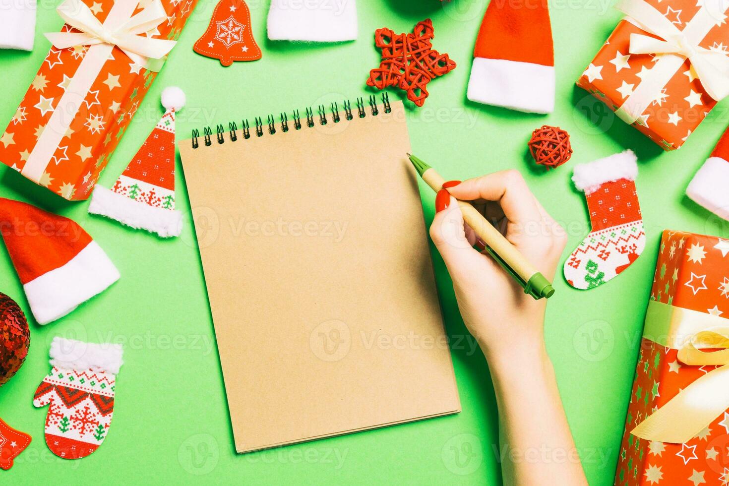 Blick von oben auf die weibliche Hand, die einige Notizen in Noteebok auf grünem Hintergrund macht. neujahrsdekorationen und spielzeug. Weihnachtszeit-Konzept foto