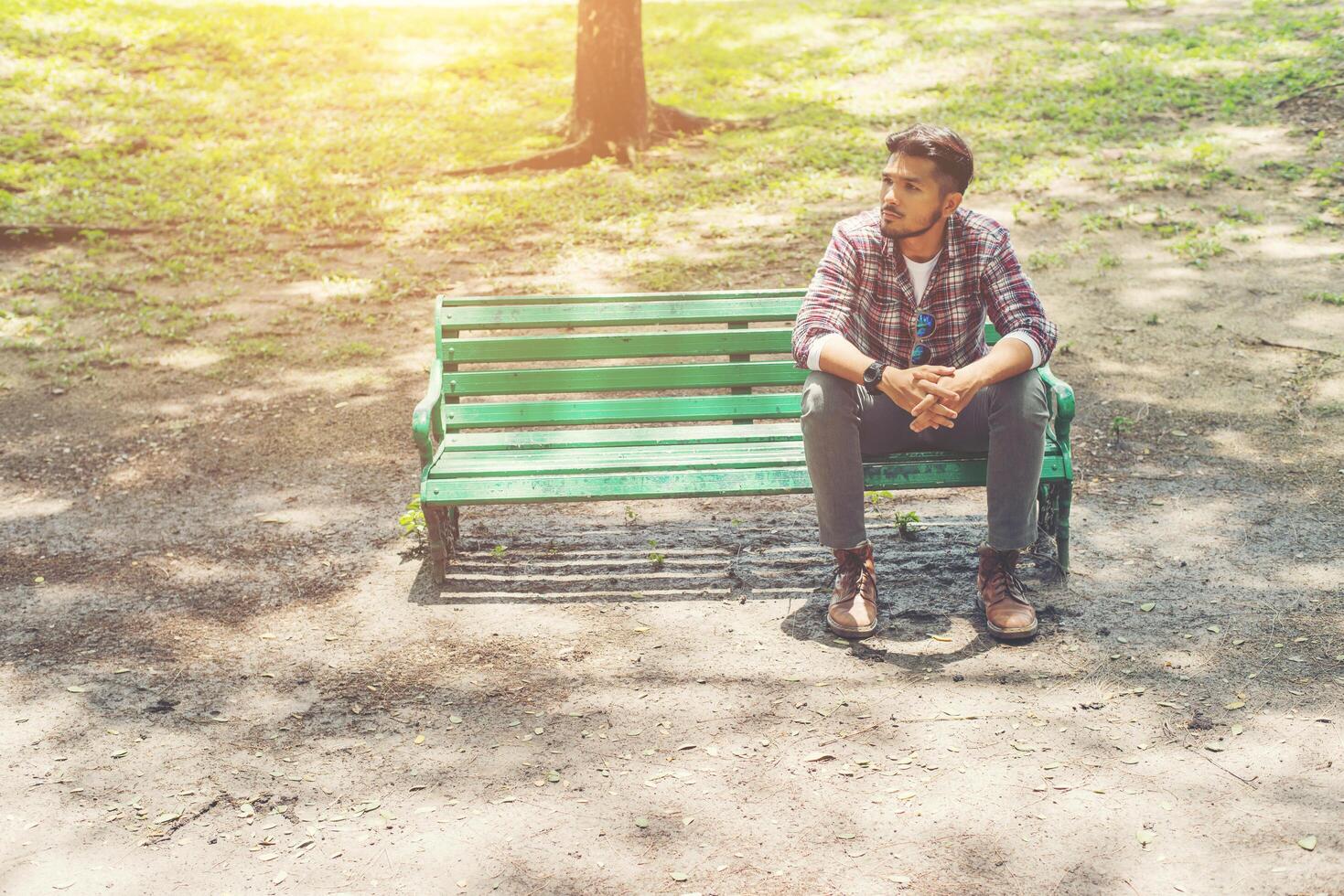 junger Hipster-Mann sitzt auf einer Holzbank im Park. foto