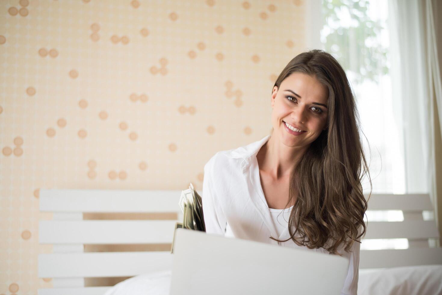 glückliche schöne Frau, die an einem Laptop auf dem Bett im Haus arbeitet foto