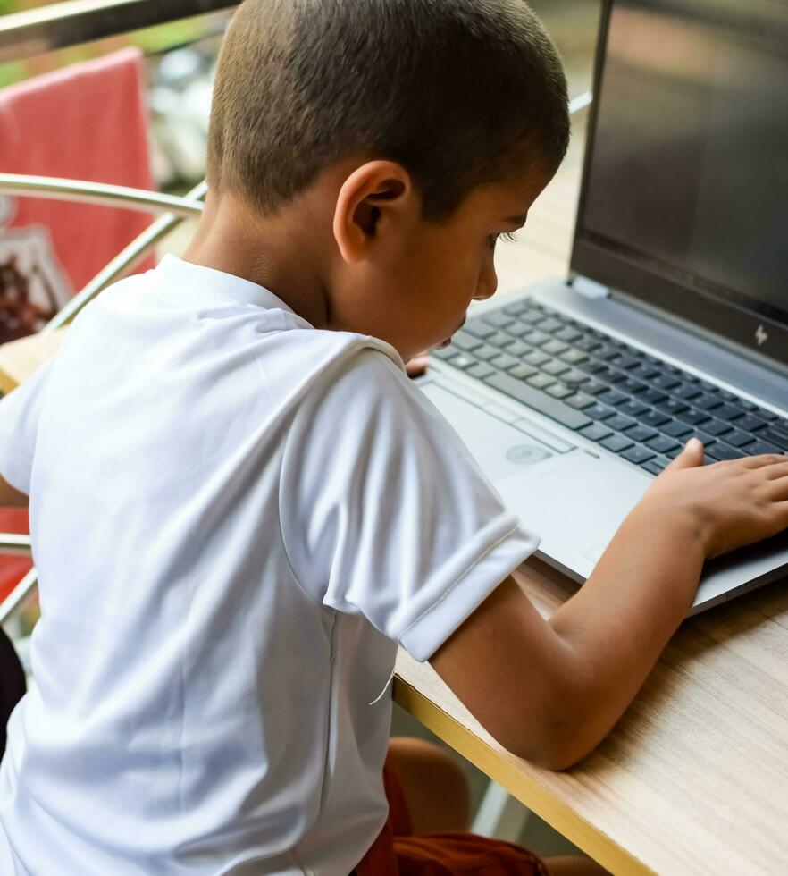 wenig Junge Sitzung beim Tabelle mit Laptop zum online Klasse im Klasse 1, Kind studieren auf Laptop von Zuhause zum Entfernung Lernen online Ausbildung, Schule Junge Kinder Lebensstil Konzept foto