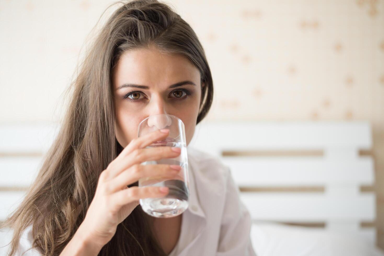 schöne Frau, die morgens frisches Wasser im Bett trinkt foto