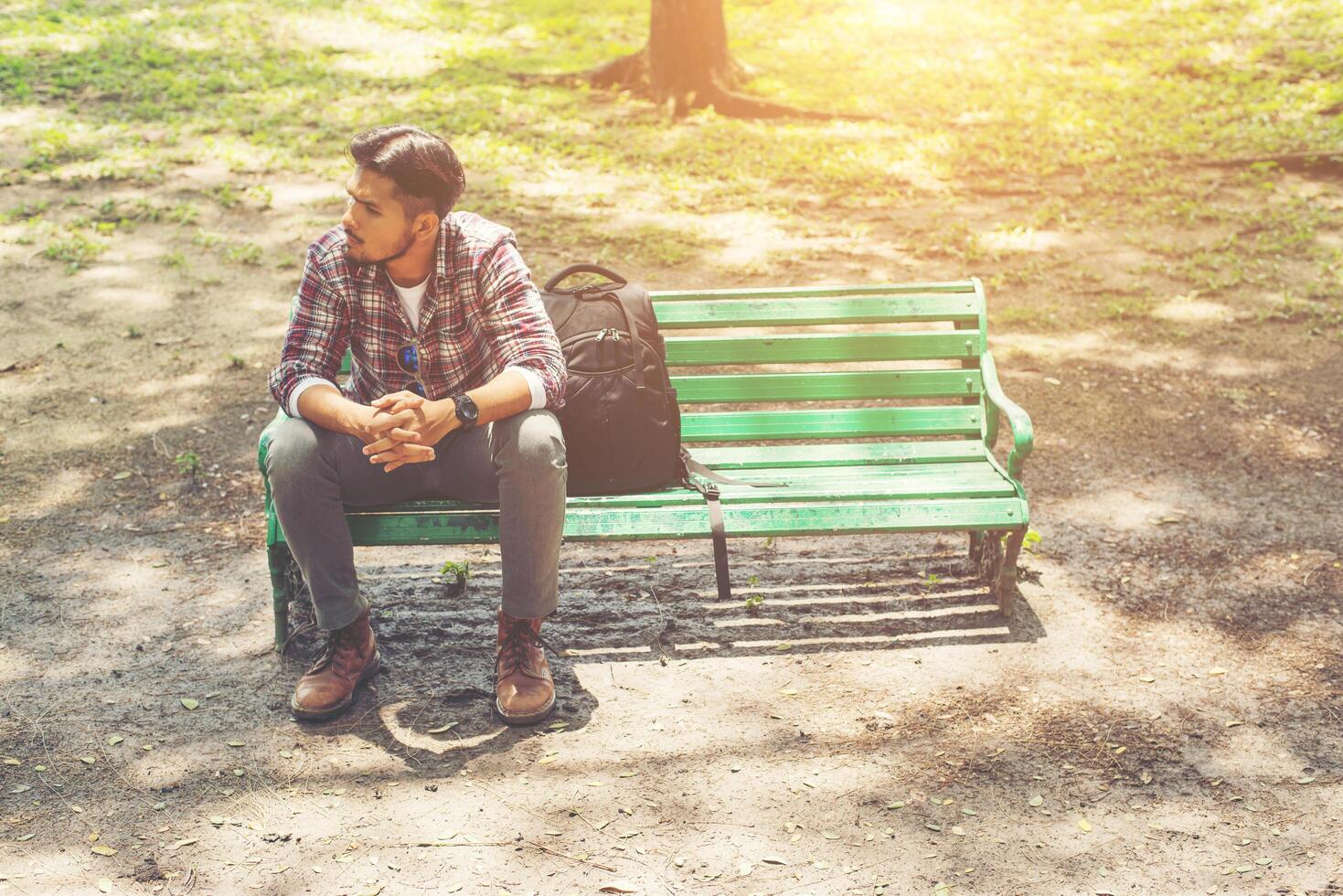 junger Hipster-Mann mit Rucksack neben dem Sitzen auf einer Holzbank. foto
