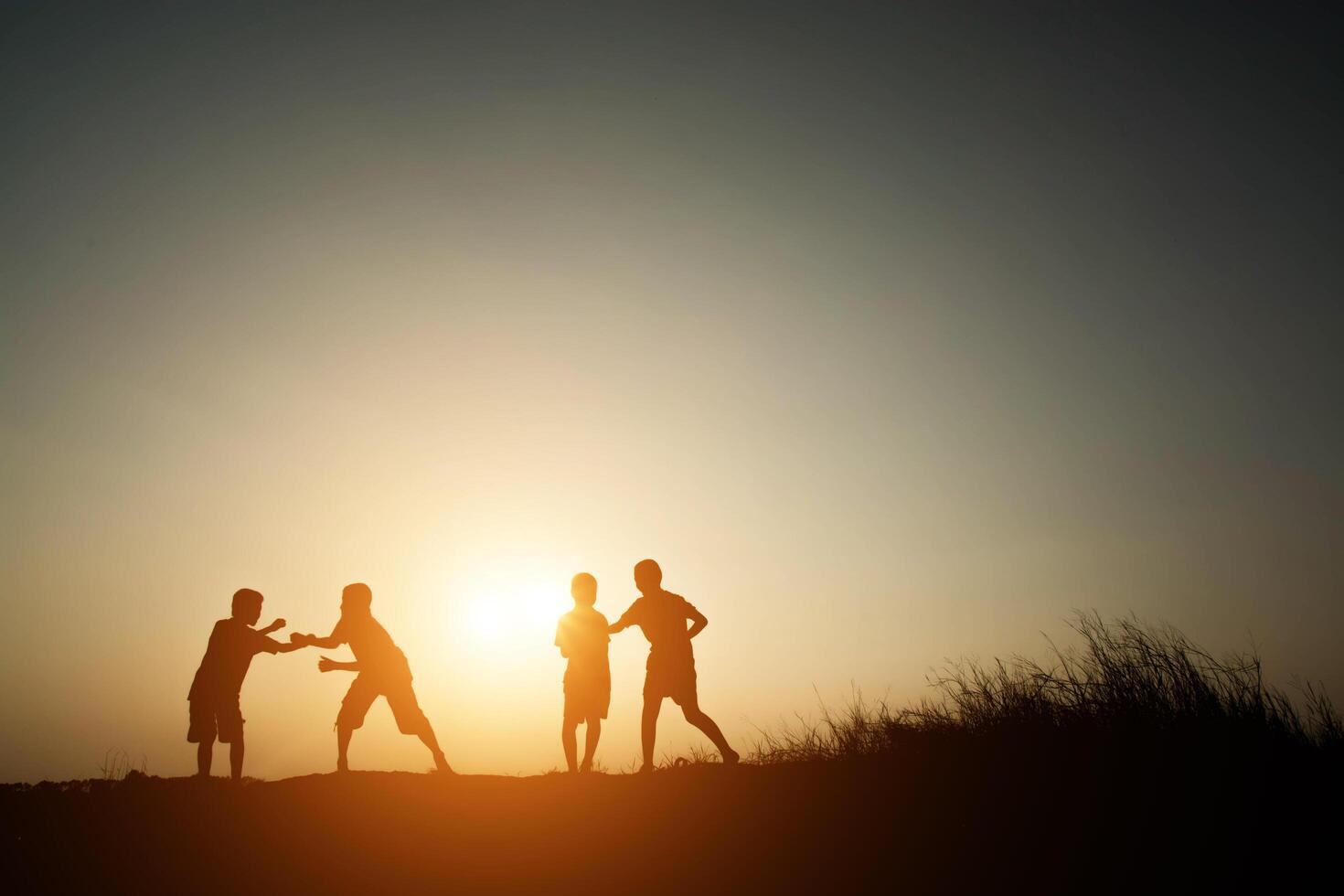 Kinder, die auf der glücklichen Zeit des Sommersonnenuntergangs spielen foto