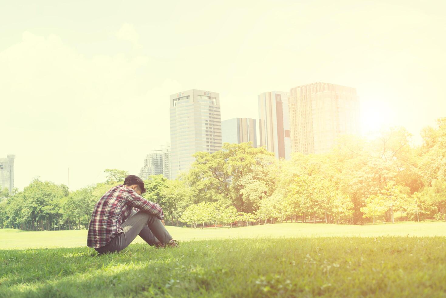 Rückansicht des entspannten jungen reisenden Mannes, der auf Gras im Park sitzt. foto