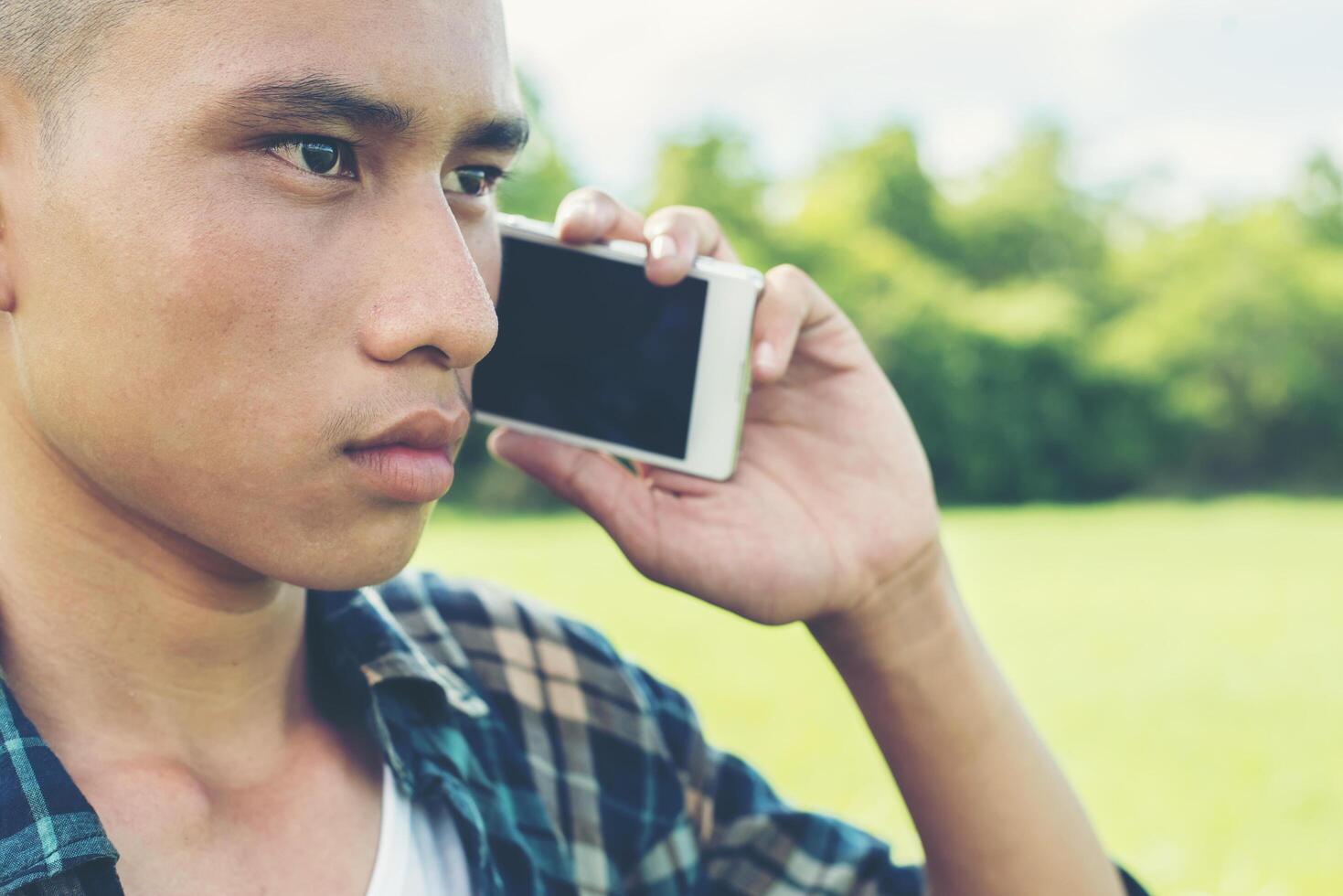 junger Mann, der am Telefon spricht und auf dem Gras im Park steht. foto